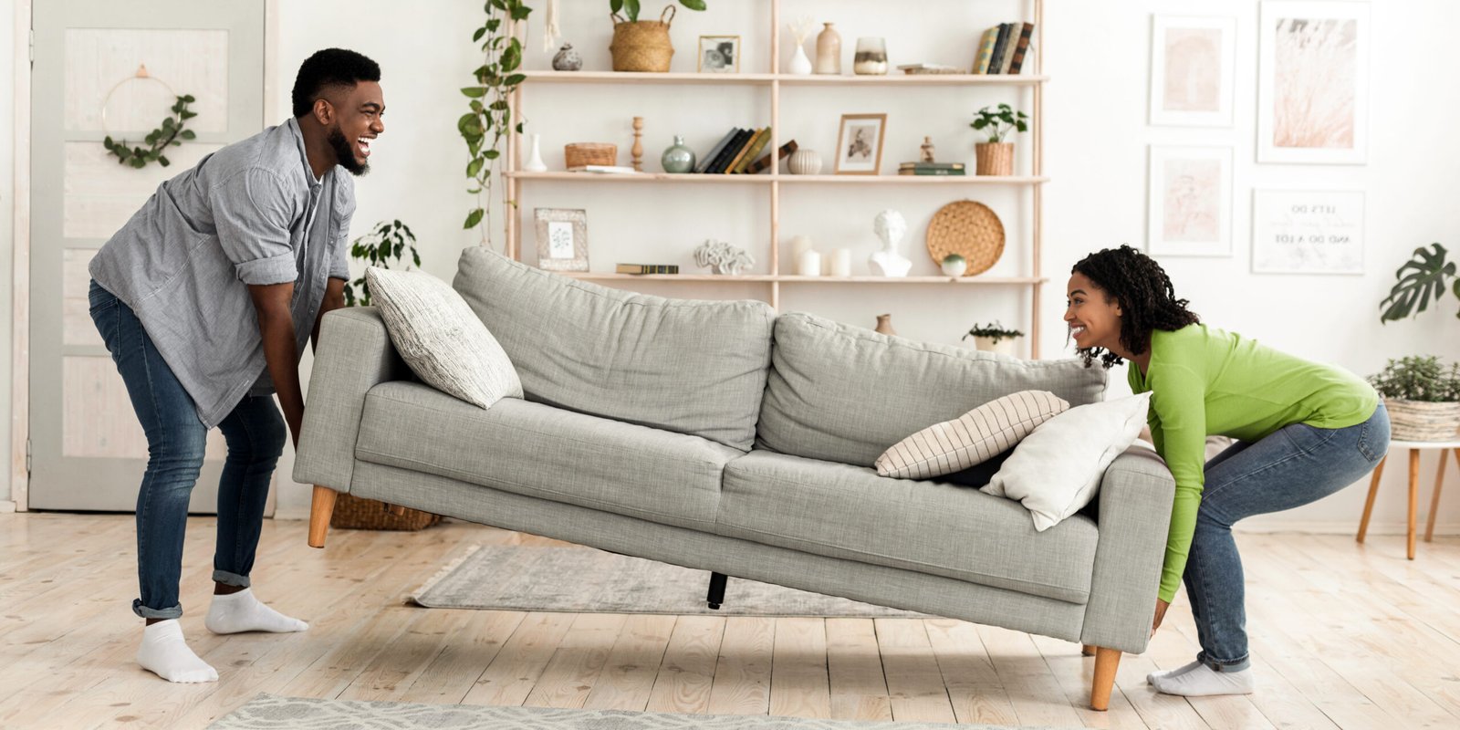 Happy african american couple moving sofa in living room, replacing furniture at home, side view